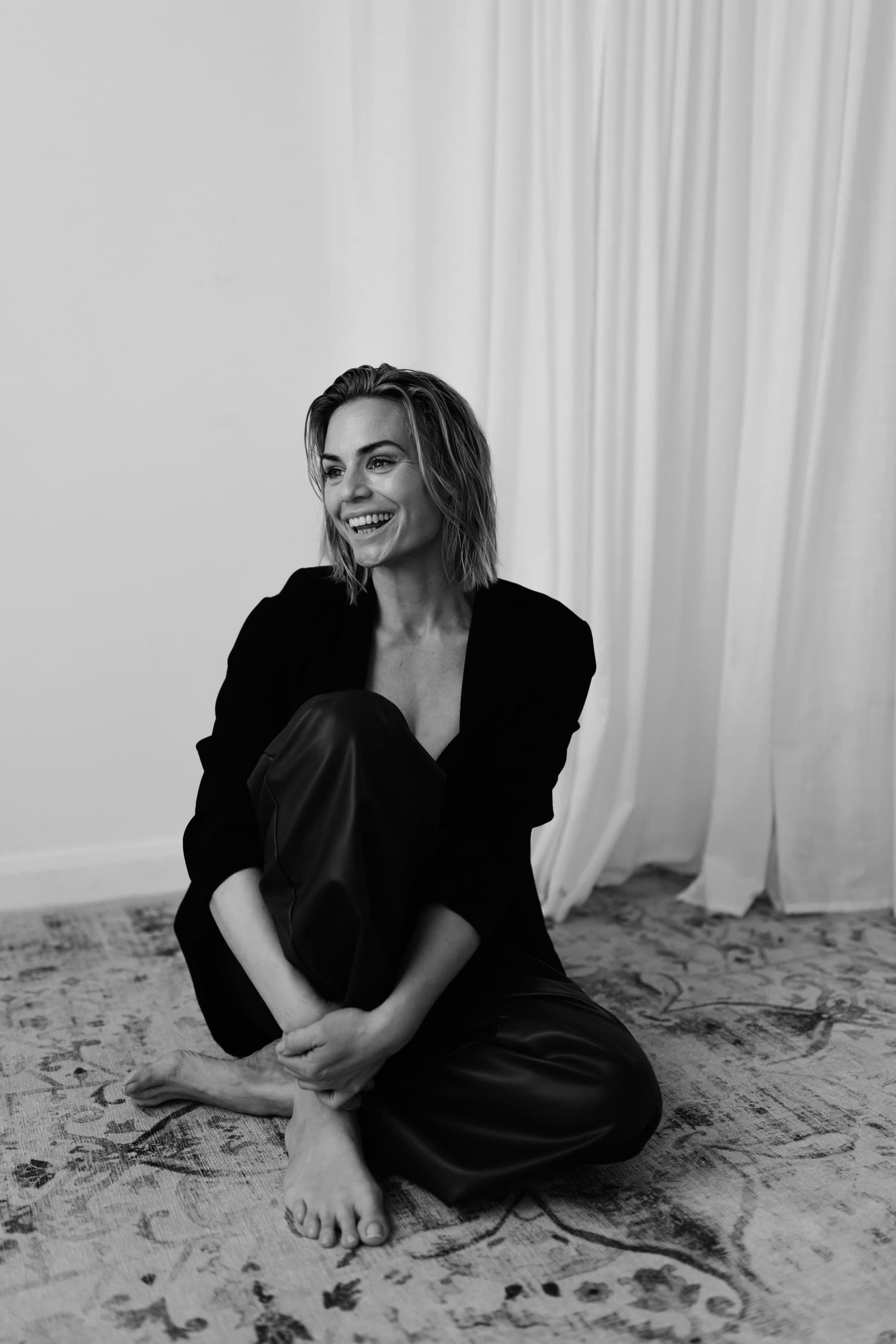 Amanda Brooke, seated and laughing, photographed in black and white